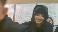 a woman wearing a hooded jacket is smiling in front of a white board that says thanks to