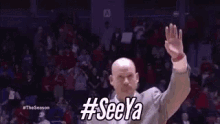 a bald man is waving his hand in the air in front of a crowd .