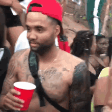 a shirtless man in a red hat holds a red cup in his hand