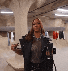 a woman in a black leather vest is standing in a room with clothes hanging on a wall