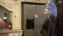 a woman in a blue wig is standing next to a refrigerator in a kitchen .