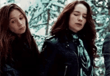 two young women are standing next to each other in a forest .