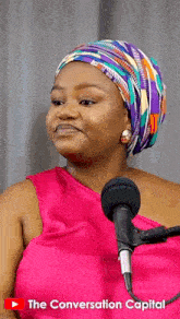 a woman wearing a head scarf stands in front of a microphone with the conversation capital written on the bottom right