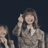 a young woman wearing a plaid jacket and a microphone points to herself