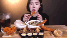 a woman is sitting at a table eating sushi and fried food