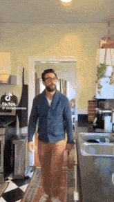 a man in a blue jacket and brown pants is walking in a kitchen with a tiktok logo on the bottom