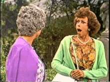 a woman in a green cardigan is talking to an older woman in a purple sweater