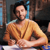 a man in a yellow shirt is writing on a notebook