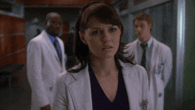 a woman wearing a headband stands in a hallway with two doctors