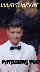 a man in a white suit with a black bow tie is on a red carpet