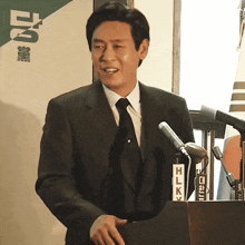 a man in a suit and tie stands behind a podium with a sign that says hlk on it