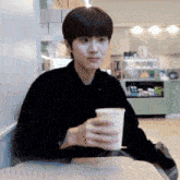 a young man is sitting at a table holding a cup of coffee .