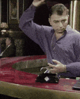 a man in a purple shirt stands at a bar holding a glass