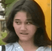 a close up of a woman 's face with long black hair and a blue shirt .