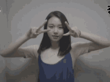 a woman in a blue tank top is making a peace sign with her fingers