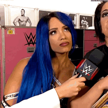 a woman with blue hair is holding a microphone with the letters w on it