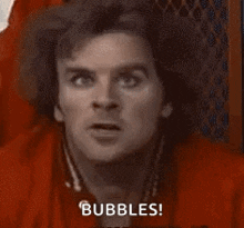 a man in a red shirt is sitting in a chair and says `` bubbles '' .