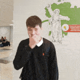 a young man covering his mouth in front of a statue of a woman holding a sword