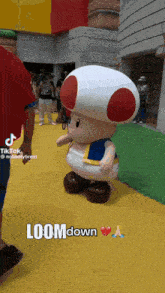 a toad mascot is standing on a yellow floor with loom down written on the bottom