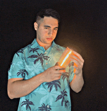 a man in a blue shirt with palm trees on it is holding a light