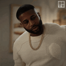 a man with a beard wearing a white sweater and a gold chain around his neck