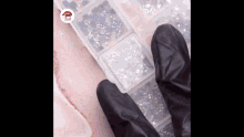 a person wearing black gloves is standing next to a box of rhinestones