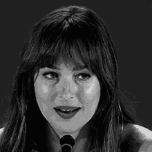 a black and white photo of a woman singing into a microphone with her eyes closed .