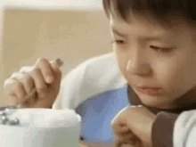 a young boy is eating a bowl of food with a fork and knife .