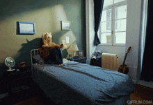 a gif from gifrun.com shows a woman sitting on a bed reading