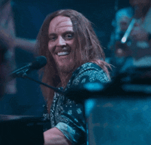 a man with long hair and a beard is smiling in front of a microphone