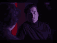 a man and a woman are looking at each other in a dark room . the woman is wearing a purple sweater .