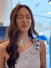 a woman with long hair is wearing a white one shoulder dress and making a funny face .