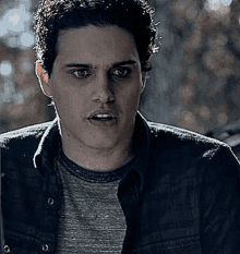 a man with curly hair is wearing a denim jacket and a gray t-shirt .