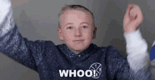 a young boy in a blue sweater is raising his arms in the air and saying whoo .
