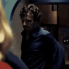 a man with curly hair and a beard is standing in a dark room looking at a woman .