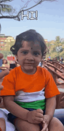 a little girl wearing an orange white and green shirt is sitting on a bench .