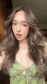 a woman in a green dress takes a selfie with her hair blowing in the wind