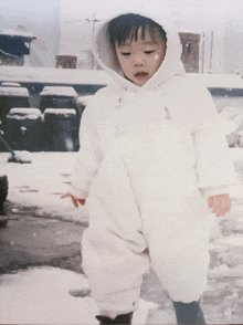 a child wearing a white jumpsuit with a hood is walking in the snow