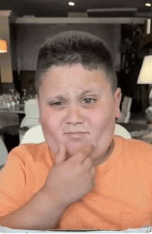 a young boy in an orange shirt is making a funny face with his hand on his chin