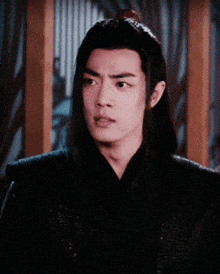 a man with long black hair and a red ponytail looks at the camera