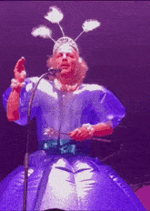 a man in an inflatable dress is singing into a microphone while wearing a tiara