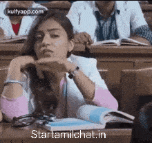 a woman is sitting at a desk in a classroom with her hands on her head .