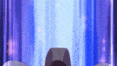 a person is standing in front of a blue curtain with a purple light coming out of it .
