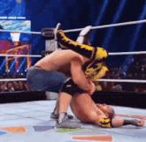 two men are wrestling in a ring and one of them is wearing a yellow and black outfit .