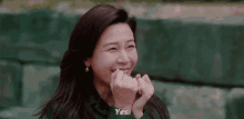 a woman is smiling and making a heart shape with her hands while sitting on a bench .