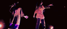 two women are singing into microphones on a stage in a dark room