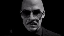 a bald man with a mustache is wearing sunglasses and a ring on his finger