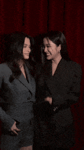 two women in suits are laughing with one covering her mouth