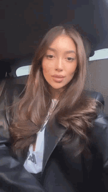 a woman with long brown hair is sitting in the back seat of a car taking a selfie .