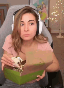 a woman wearing headphones holds a box of food in her hand